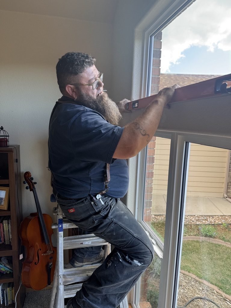 Austin of Pre-Listing Pros leveling a curtain rod at a bright window in a Northern Colorado home